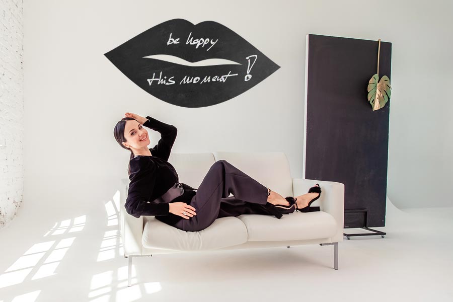 schöne brünette liegt auf dem sofa vor einer wand mit tafelfolienmotiv kussmund